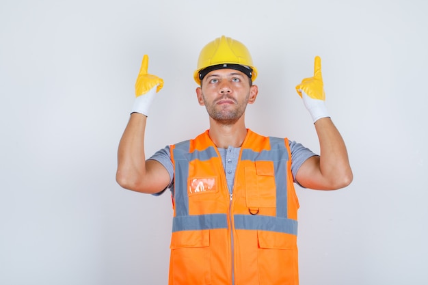 Строитель-мужчина, подняв указательные пальцы вверх в строительной форме спереди.