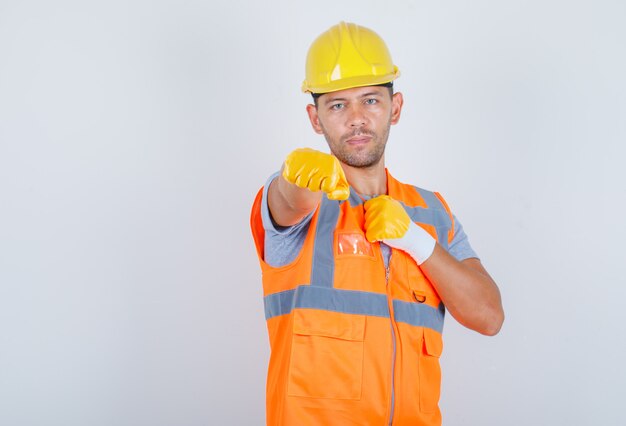 Male builder showing fists as boxer in uniform, helmet, gloves and looking serious, front view