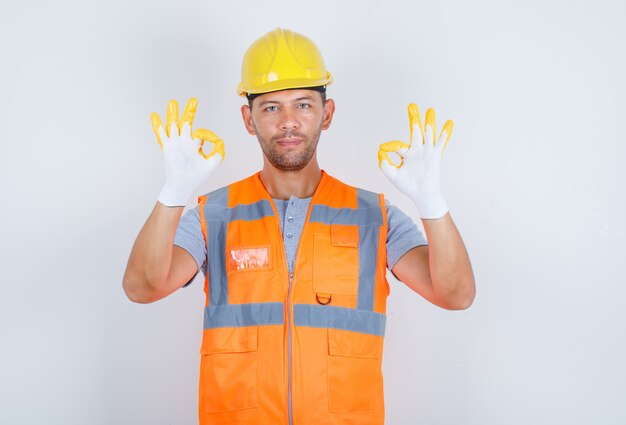 Male builder showing ok sign with hands in uniform and looking confident, front view.