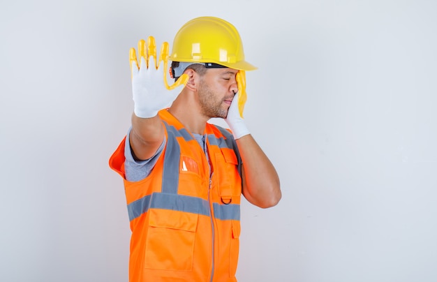 Male builder showing stop to camera in uniform, helmet, gloves, front view.