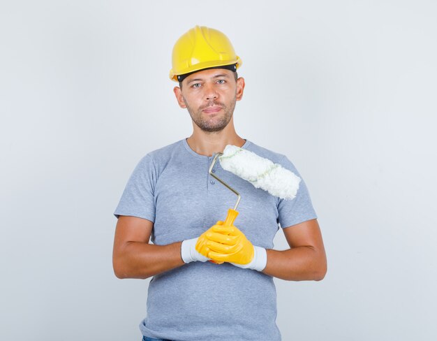 Строитель-мужчина в футболке, шлеме, перчатках с валиком, вид спереди.