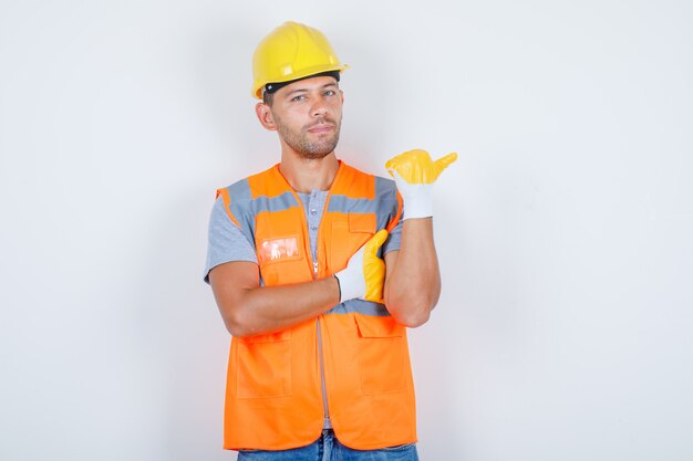 Male builder in uniform pointing away while standing and looking confident, front view.