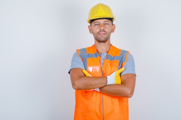 Мужчина-строитель в униформе, стоя со скрещенными руками и уверенно глядя, вид спереди.