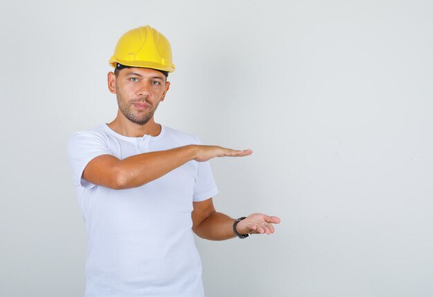 Male builder in white t-shirt, security helmet showing large size gesture, front view.