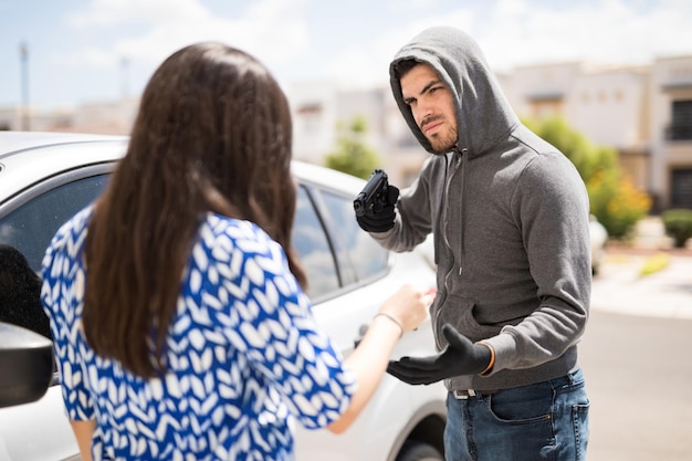 Male burglar robbing a car from a young woman while pointing a gun at her