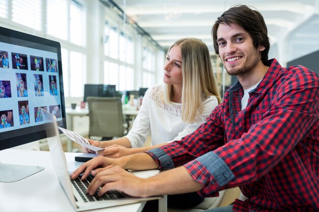 Male business executive working on laptop while coworker looking at computer