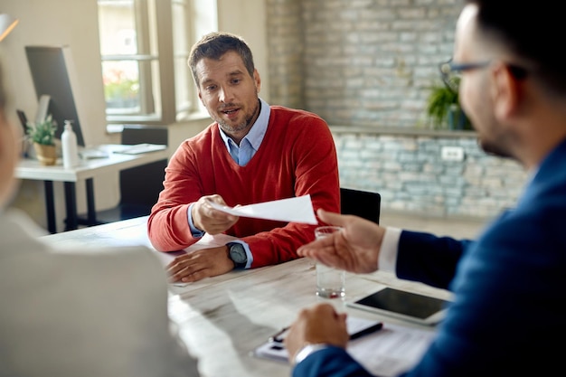 Foto gratuita candidato maschio che dà il suo cv a un membro del team delle risorse umane mentre ha un colloquio di lavoro in ufficio