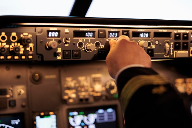 Male captain fixing altitude and longitude level on dashboard in plane cockpit. Pilot pushing buttons on control panel switch, using windscreen in aircraft cabin to fly airplane. Close up.