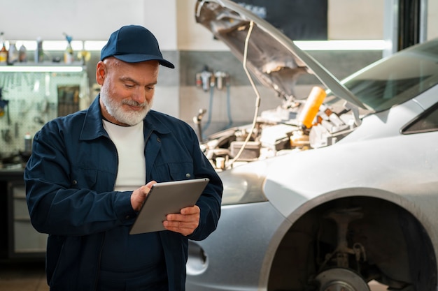 Foto gratuita meccanico di automobile maschio che utilizza il dispositivo della compressa nell'officina di riparazione dell'automobile