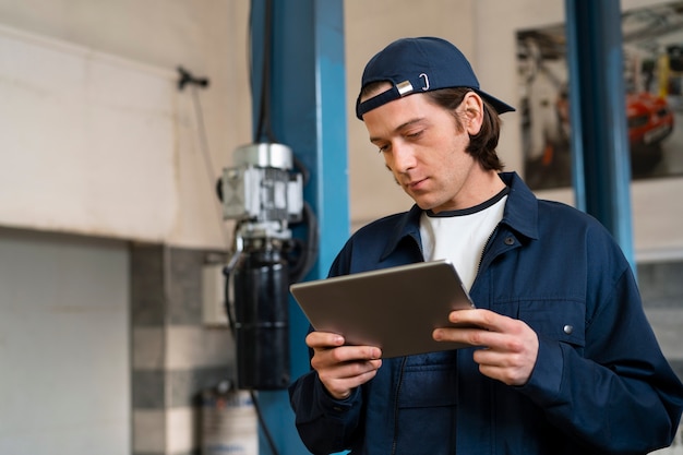 Foto gratuita meccanico di automobile maschio che utilizza il dispositivo della compressa nell'officina di riparazione dell'automobile