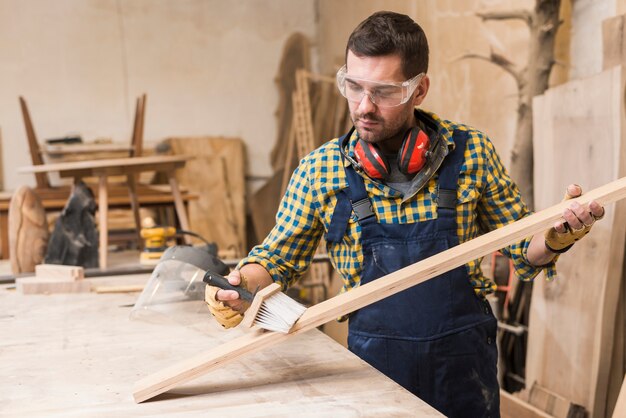 Male carpenter cleaning the plank with brush