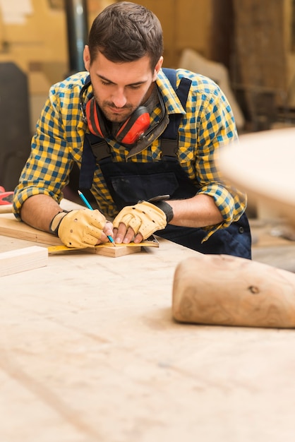 Carpentiere maschio che misura il blocco di legno con il righello e la matita