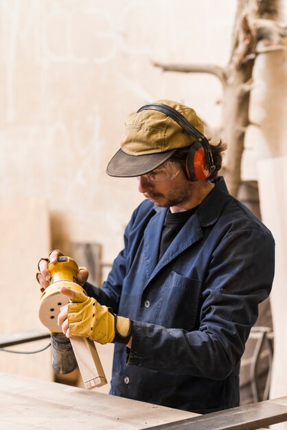 Male carpenter processes the block with a random orbit sander in the workshop