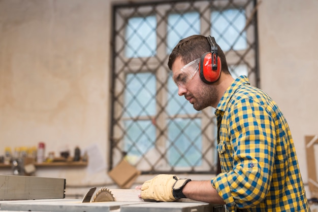Free photo male carpenter wearing safety glasses and ear defender cutting the block on circular saw blade