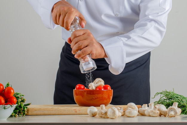 Foto gratuita cuoco unico maschio che aggiunge sale negli alimenti in cucina in uniforme e grembiule