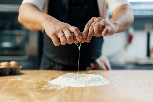 男性シェフが小麦粉の上で卵を割る