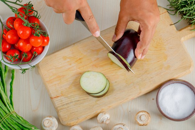 Male chef chopping eggplant on wooden board in kitchen