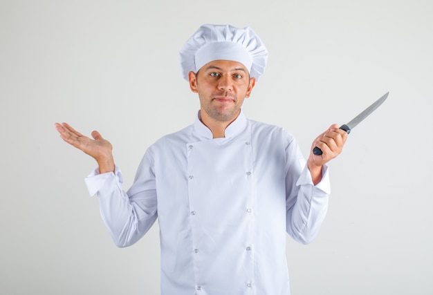 Cuoco maschio del cuoco unico in coltello della tenuta del cappello e uniforme e sembrare sconcertante