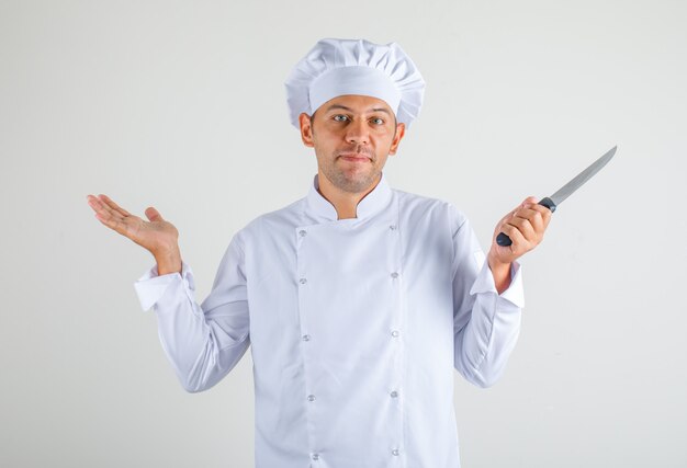 Male chef cook in hat and uniform holding knife and looking confused