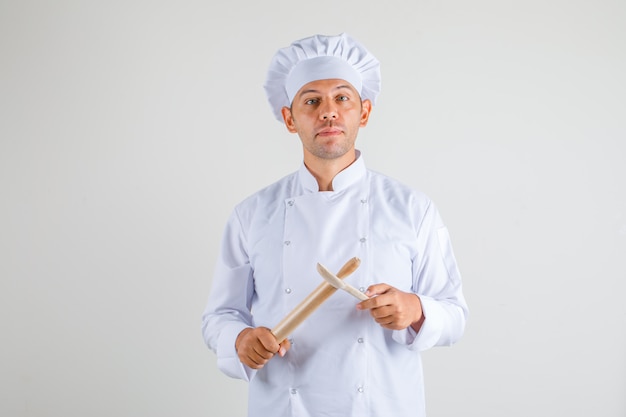 男性シェフが帽子と麺棒と木のスプーンを保持している制服で調理します。