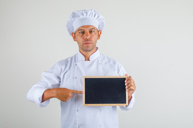 Male chef cook pointing finger at blackboard in hat and uniform