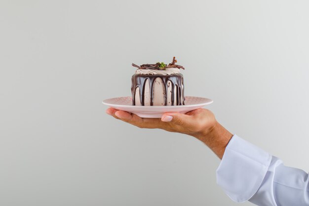 Мужской шеф-повар в форме проведения десерт торт в тарелку