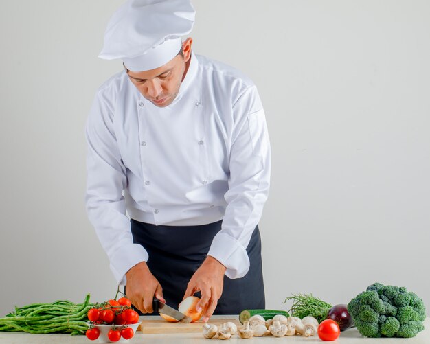 부엌에서 유니폼, 앞치마와 모자에 나무 보드에 남자 요리사 절단 양파