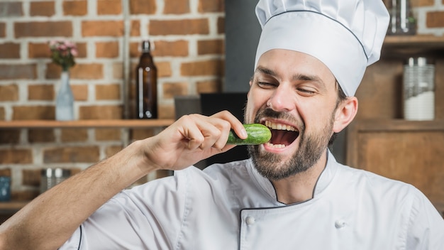 Male chef eating fresh cucumber in the kitchen