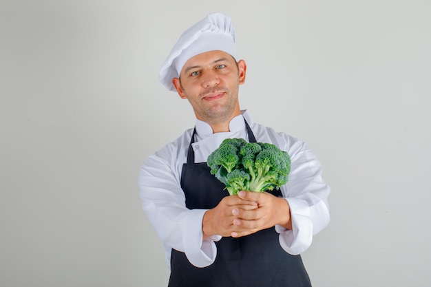 Male chef in hat, apron and uniform holding broccoli and smiling