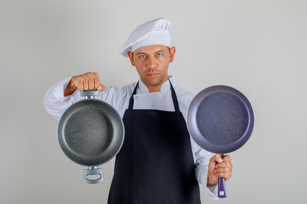 Male chef in hat, apron and uniform holding empty pans