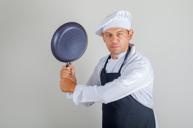 Мужской шеф-повар в шляпе, фартуке и форме держит сковороду, весело проводя время