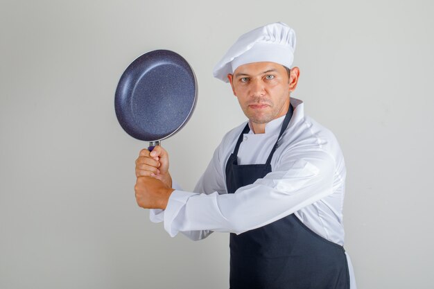 Male chef in hat, apron and uniform holding frying pan while having fun