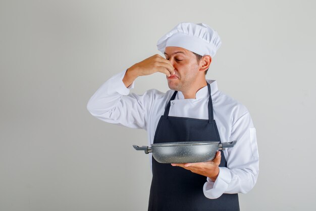 Male chef holding bad dish and closing nose in hat, apron and uniform