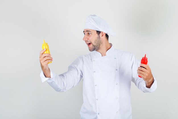 Male chef holding bottles of ketchup and mustard in white uniform
