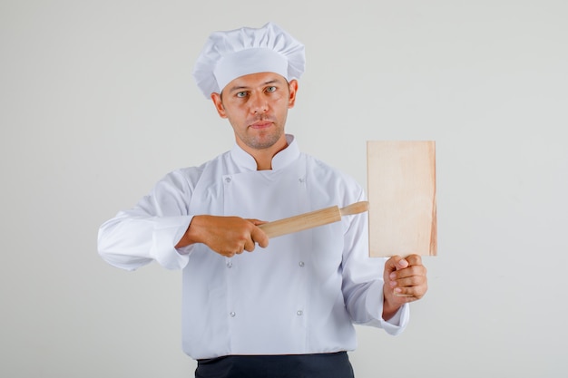 Male chef holding cutting board and rolling pin in uniform, apron and hat