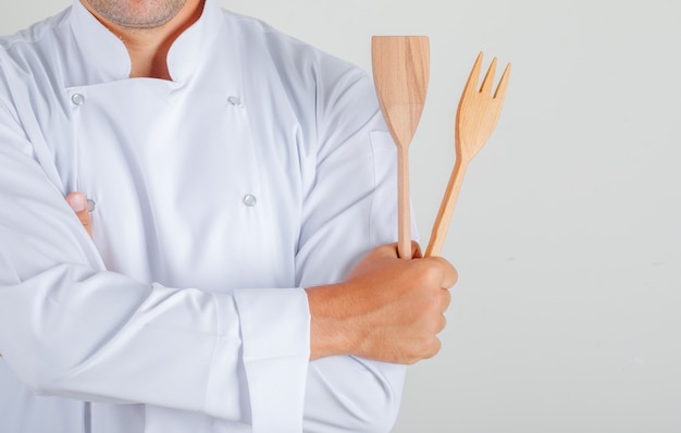 Male chef holding kitchen utensils with crossed arms in uniform