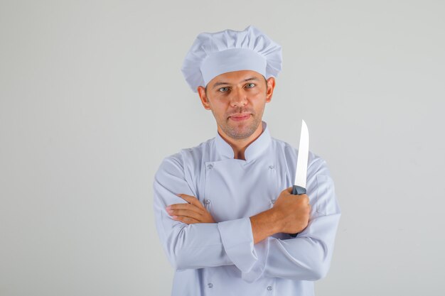 Мужской шеф-повар держит нож со скрещенными руками в форме и шляпе и выглядит уверенно
