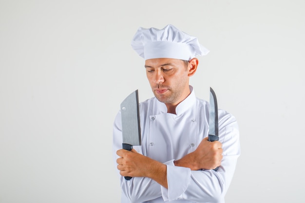 Foto gratuita cuoco unico maschio che tiene i coltelli con le braccia incrociate in uniforme e cappello