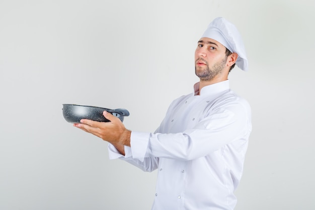 Male chef holding pan in white uniform and looking proud