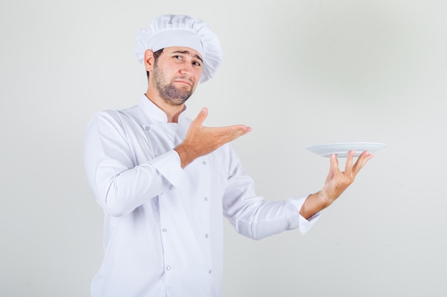 Male chef holding plate in white uniform and looking displeased.