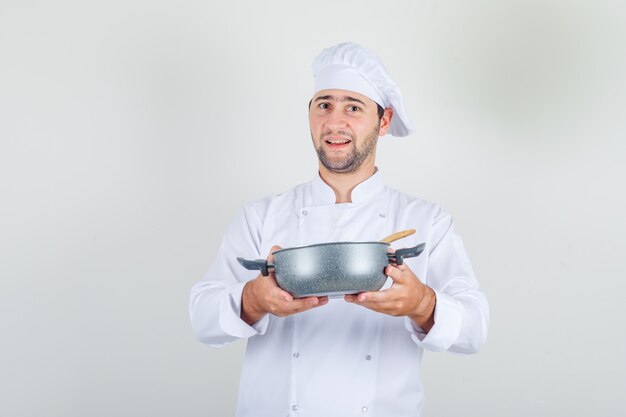 Бесплатное фото Шеф-повар-мужчина держит суп в кастрюле в белой форме и выглядит счастливым