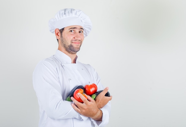 Male chef holding tomatoes and eggplant in white uniform