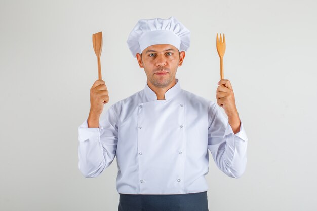 Мужской шеф-повар держит деревянные кухонные принадлежности в форме, фартук и шляпу
