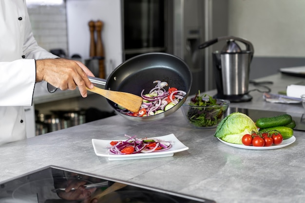 Бесплатное фото Шеф-повар на кухне наливает еду на тарелку из сковороды