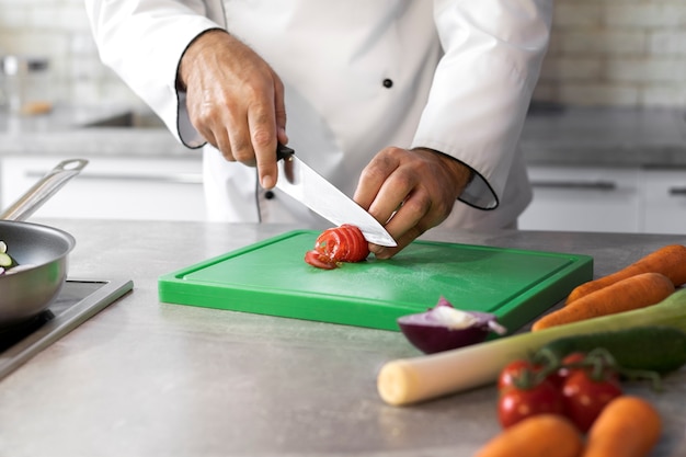 Foto gratuita cuoco unico maschio in cucina a tagliare le verdure per il piatto