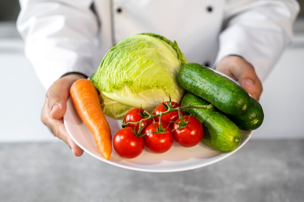 Male chef in the kitchen holding plate of fresh vegetables