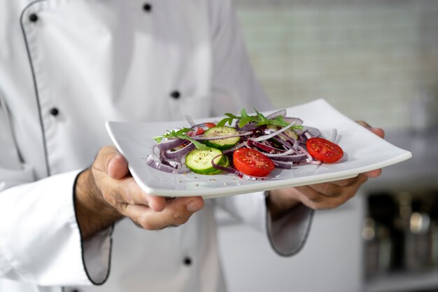 Male chef in the kitchen holding plate of salad