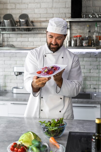 Male chef in the kitchen holding plate of salad