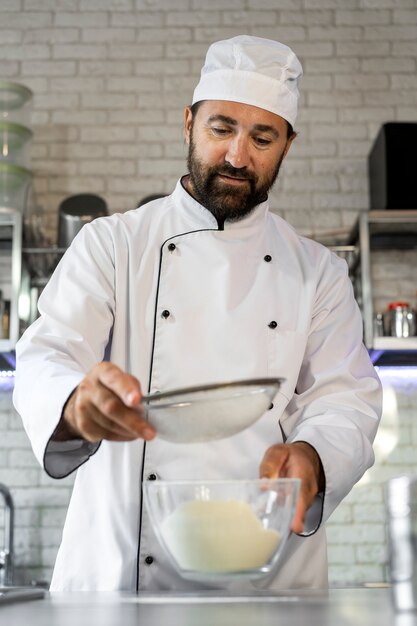 Male chef in the kitchen sifting flour