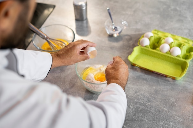 Foto gratuita cuoco unico maschio in cucina usando le uova per cucinare